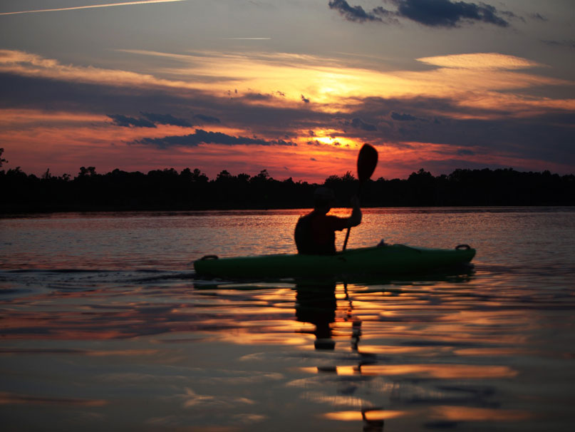 Kayakiste au coucher du soleil sur un plan d'eau landais